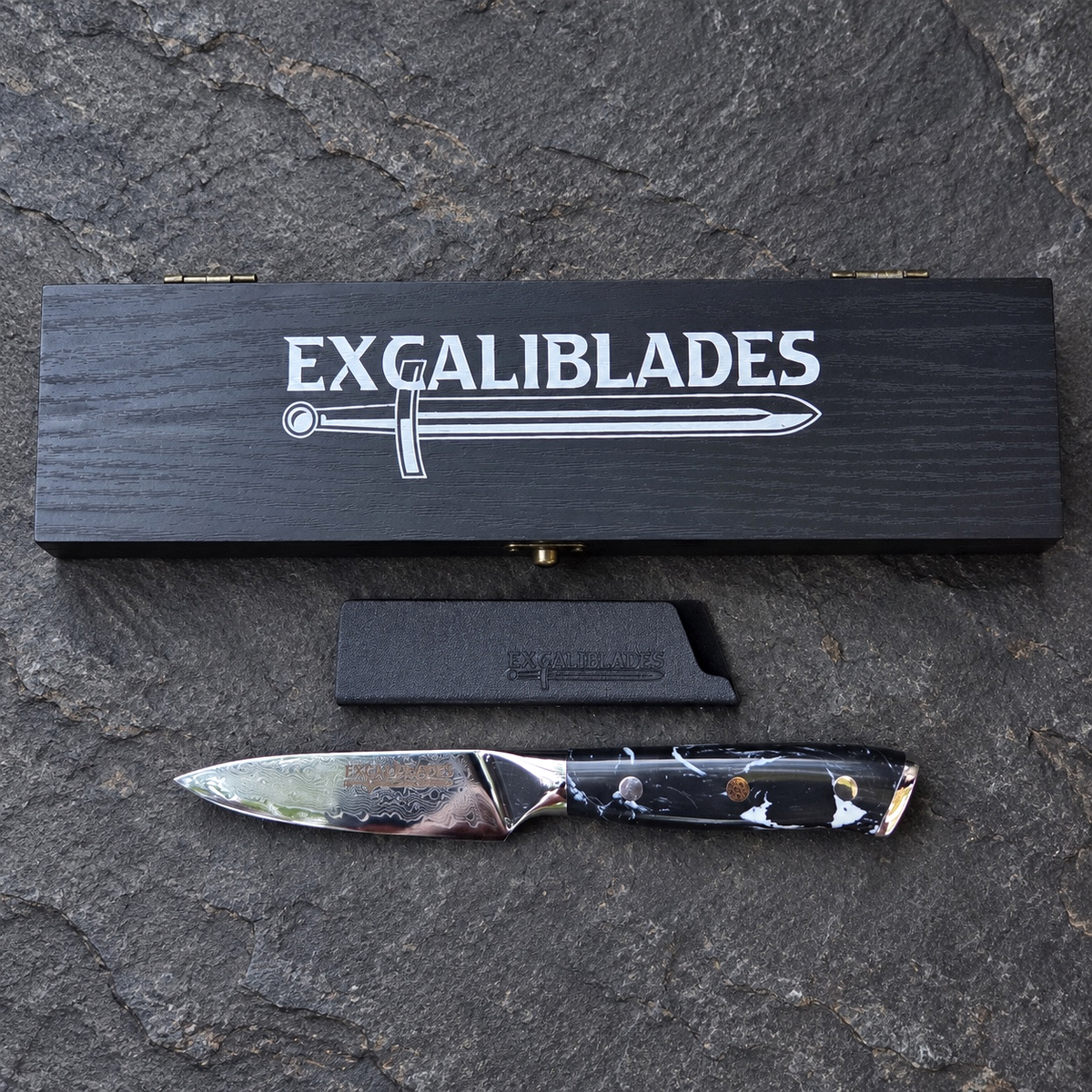 Excaliblades paring knife beside its closed black wooden gift box and protective sheath
